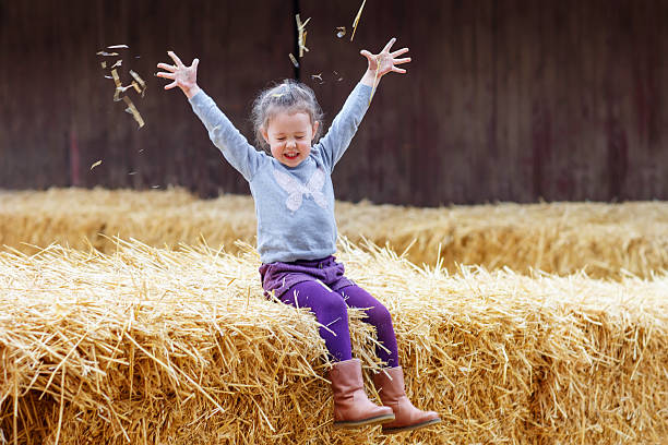 Little cute happy girl having fun with hay on a farm. Child enjoying autumn season and laughing. Happy childhood, lifestyle concept.
