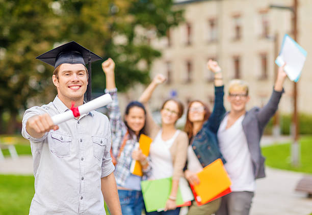 education, campus and teenage concept - smiling teenage boy in corner-cap with diploma and classmates on the back