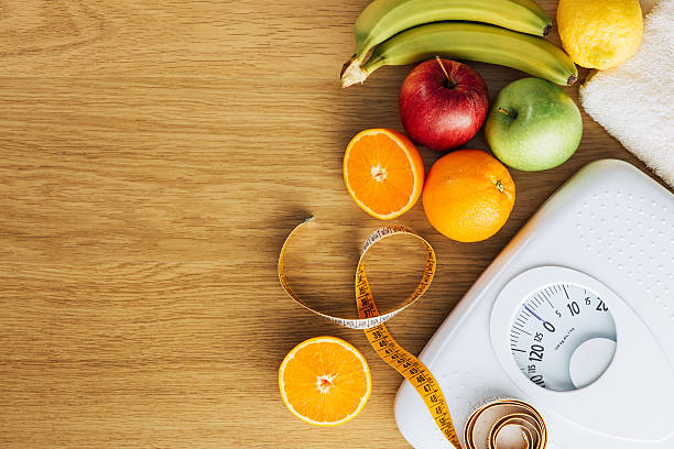 Healthy eating and weight loss concept Healthy eating, fitness and weight loss concept, white scale with fruit on a wooden table, blank copy space at left mass unit of measurement photos stock pictures, royalty-free photos & images