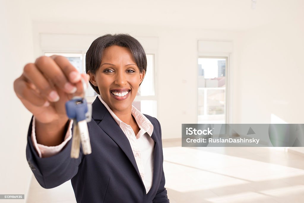 Real estate concept. Young business woman holding key of new home, showing the key to the camera , in the background new empty apartment , living room. African Ethnicity Stock Photo