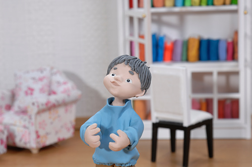 a clay doll boy looks up with a happy smile in his miniature room.