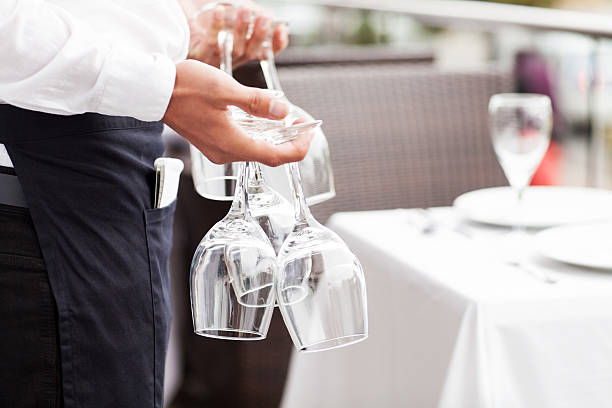 Midsection close-up of young waiter holding empty wine glasses in restaurant. Horizontal shot.