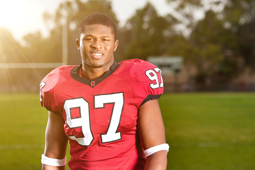 Portrait of a happy african american college football player standing on a football field in the sunlight.