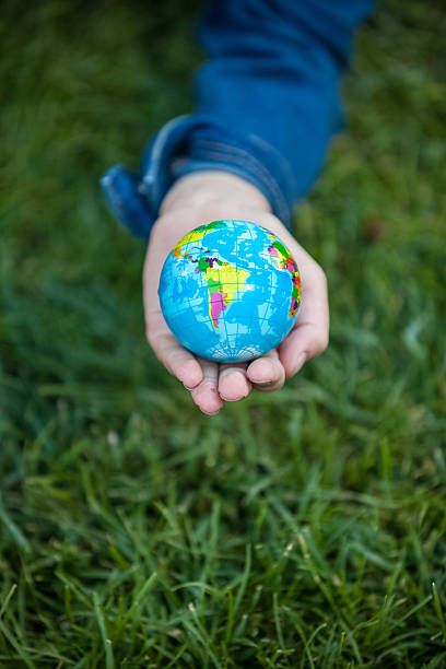 istock girl holding small Earth globe in hand against grass background 513992681