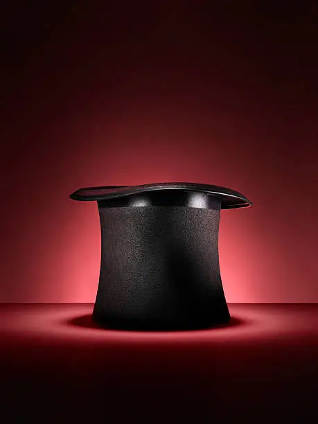 Shot of a traditional magicians style top hat set up for a trick or illusion on a red background with space left for the designer to add an object or type.