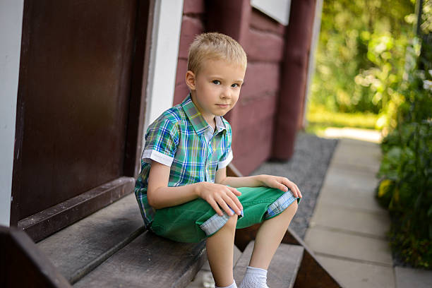Smiling young blond boy sitting on porch steps at home ?
