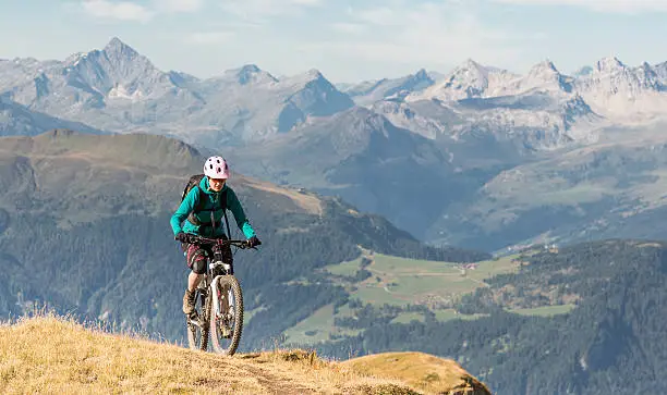 A female mountainbiker is climbing uphill in the morning on a scenic single trail high up above the village of Lenzerheide, Graubünden Canton, Switzerland.