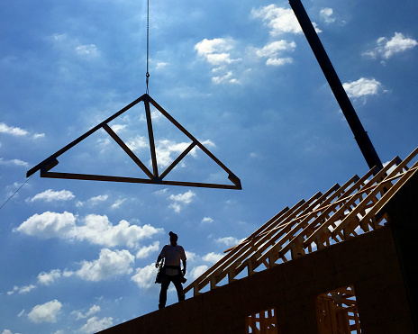 Construction worker placing roof truss onto house under construction.