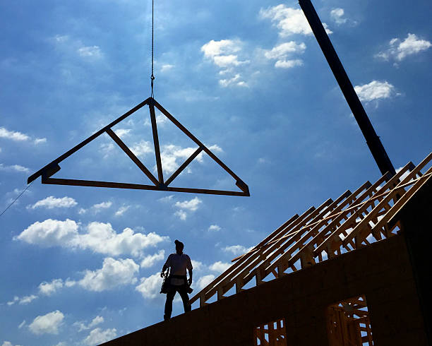 House under construction. Construction worker placing roof truss onto house under construction. timber framed stock pictures, royalty-free photos & images