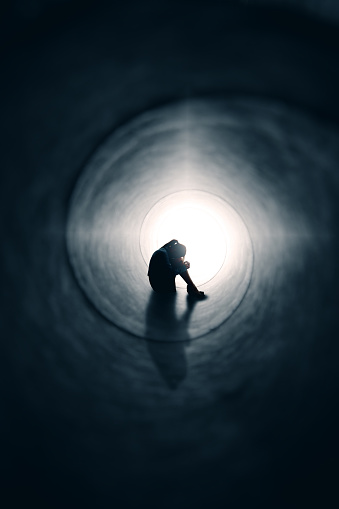 A depression concept image of a woman looking sad as she hids from the light at the end of the tunnel.