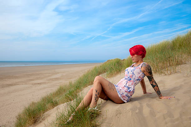 A cute redhead wearing a Summer mini-dress relaxing in a sand dune near the beach.