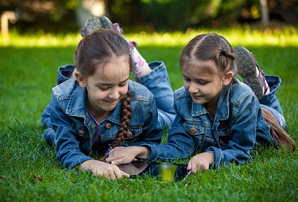 istock two small sisters with tablet lying on grass at park 514029701