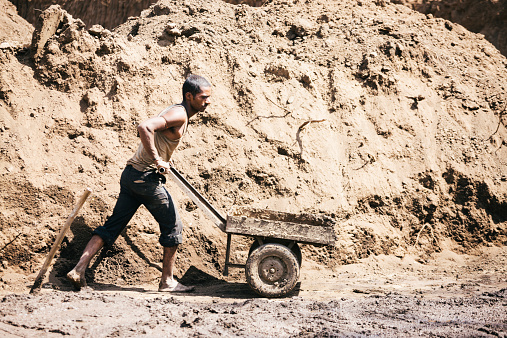 Rajasthan, India - March 13, 2014: A clay digger leans and pushes his cart, at a brick factory. Rajasthan, India