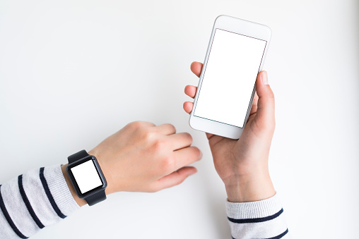 Woman wearing a smart watch, holding smart phone with other hand  on white background. Blank white screens are visible.