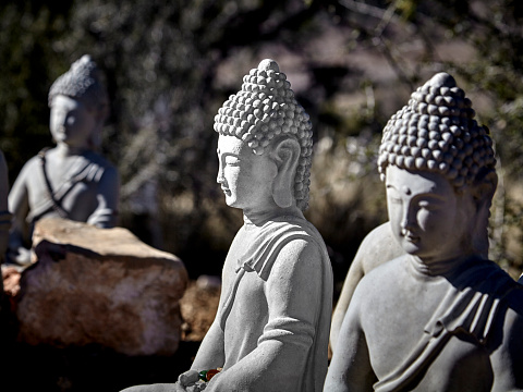 Buddhist figures made of cement sitting in meditation with prayer offerings