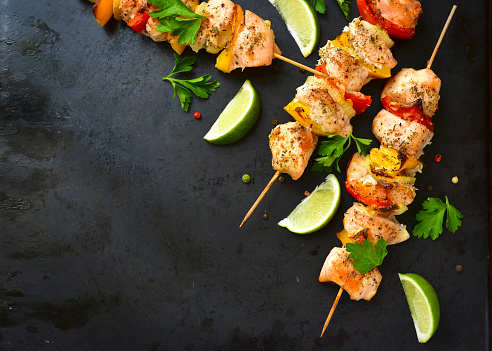 Grilled chicken kebab with vegetables on a black background.