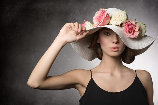 fashion summer close-up portrait of sexy brunette girl with black dress and big hat with colorful flowers, romantic spring style. she Looking in camera
