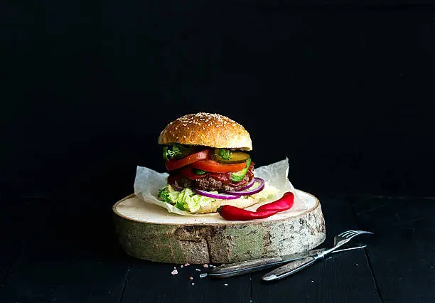 Photo of Fresh homemade burger on wooden serving board with spicy tomato