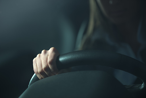 Woman driving a car late at night, hands on steering wheel close-up.