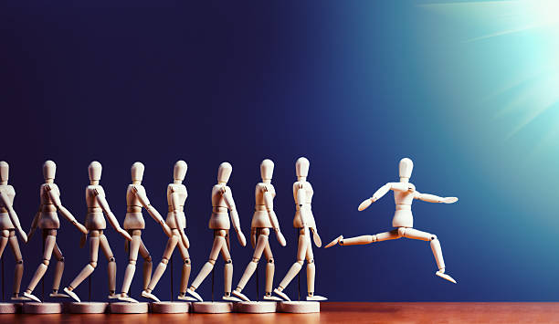 Brave puppet breaks away from pack, leaping into spotlight A single wooden lay figure leaps ahead of a line of other marionettes into the spotlight. Copy space on the dark blue background. initiative photos stock pictures, royalty-free photos & images