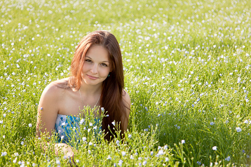 Attractive girl posing in the middle of field of flax. She squatting, looking at camera and smiling.