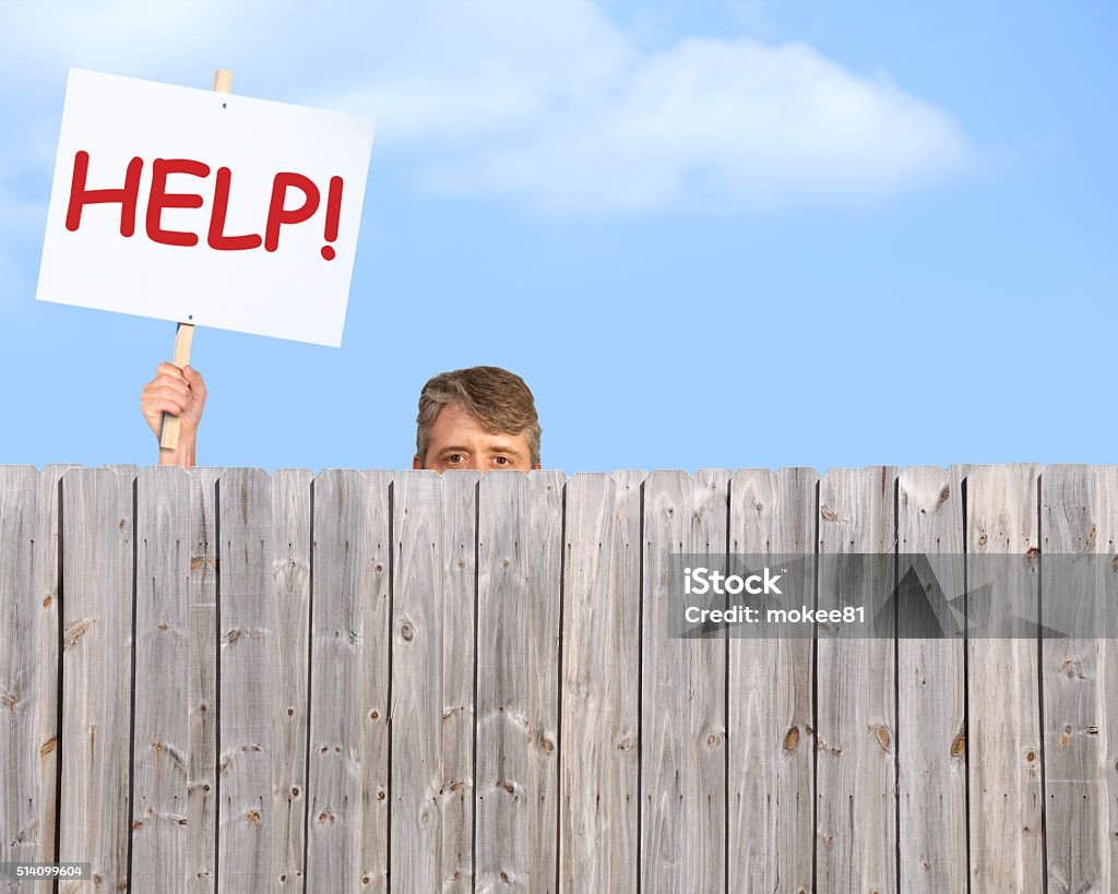 Man with HELP sign looking over wood privacy fence A man holding a HELP sign is peering over a fence desperate for help with his many problems in addiction, bipolar disorder, depression or could represent a man in need of anything imaginable. Neighbor Stock Photo
