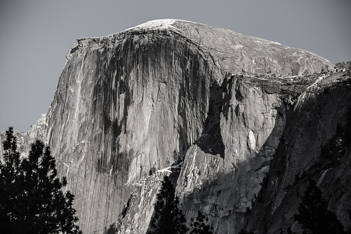 November afternoon sunlight illuminates Half Dome in Yosemite National Park, California. Color original is converted to black and white with touch of color saturation and a film grain effect to simulate an old-time analog photograph.