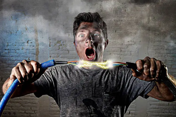 young untrained man joining electrical cable suffering domestic accident with dirty burnt face in funny shock expression screaming crazy in electricity DIY repairs danger concept