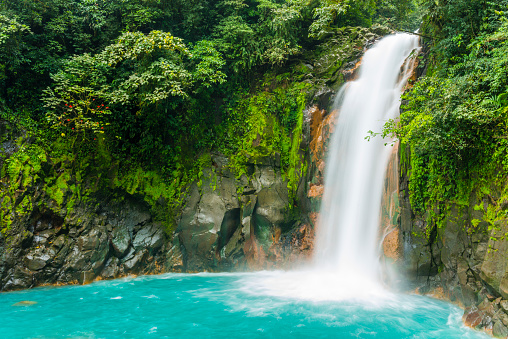 This is a horizontal, royalty free stock photograph of scenic Costa Rica, a Central American travel destination. The Rio Celeste waterfall is a natural landmark for eco tourists visiting Tenorio National Park. The flowing water falls over a rocky cliff, through green rainforest vegetation, and pools into an aqua color at the base. Photographed with a Nikon D800 DSLR camera.