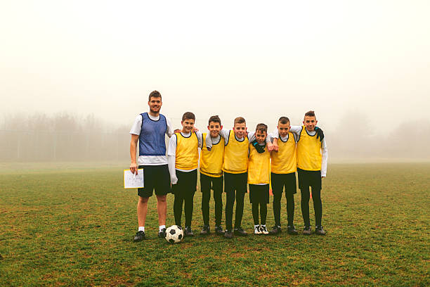 Portrait of Kids Team With Coach After Playing soccer Children playing soccer. Group photo after training or game with their coach. They are smiling and having training with their coach on foggy, cold, winter morning. They are dedicated to become a new soccer stars. Looking at camera and smiling. youth sports competition stock pictures, royalty-free photos & images