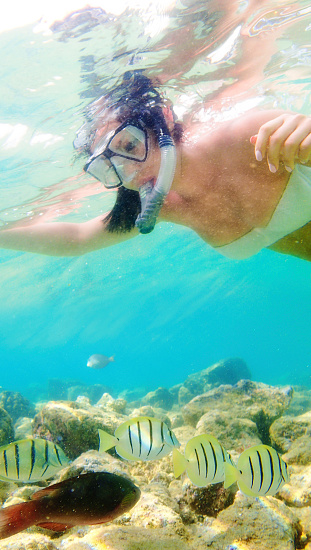 Woman in bikini swimsuit, snorkeling with reef fishes in the tropical beach.