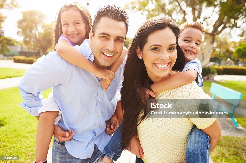 Parents Giving Children Piggyback Ride In Garden Parents Giving Children Piggyback Ride In Garden Smiling To Camera Family Stock Photo