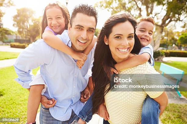 Parents Giving Children Piggyback Ride In Garden Stock Photo - Download Image Now - Family, Latin American and Hispanic Ethnicity, Happiness