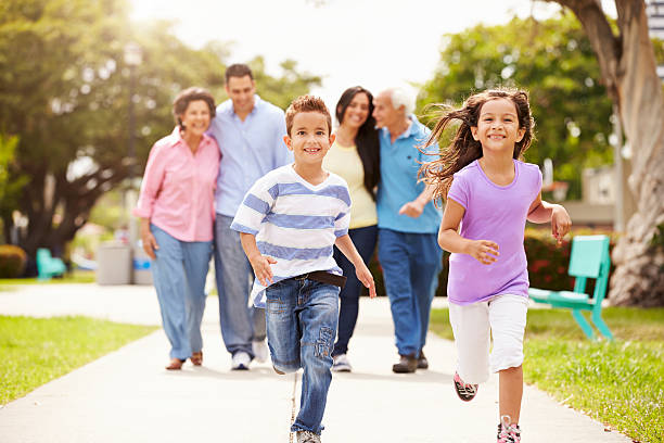 Multi Generation Family Walking In Park Together Multi Generation Family Walking In Park Together Children Running Ahead hispanic family stock pictures, royalty-free photos & images