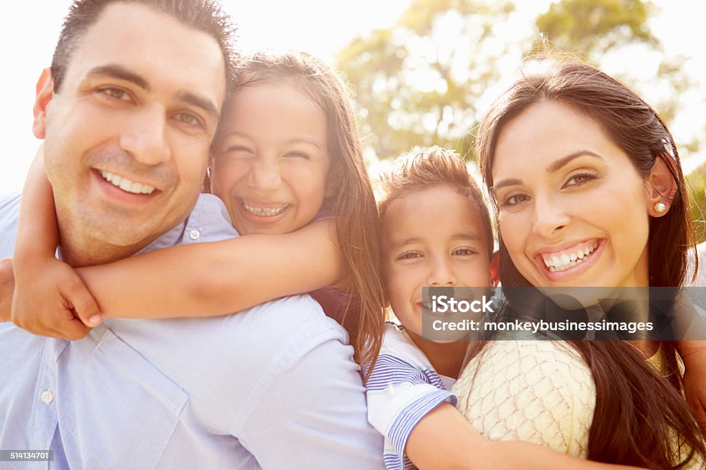 Parents Giving Children Piggyback Ride In Garden Parents Giving Children Piggyback Ride In Garden Smiling To Camera Family Stock Photo