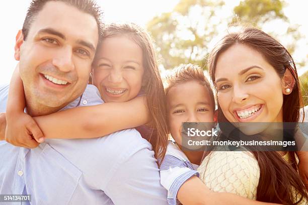 Parents Giving Children Piggyback Ride In Garden Stock Photo - Download Image Now - Family, Latin American and Hispanic Ethnicity, Smiling