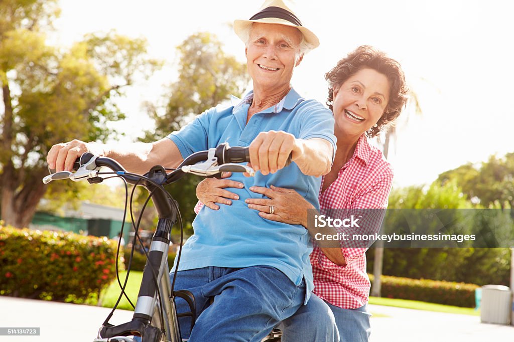 Senior Hispanic Couple Riding Bikes In Park Senior Hispanic Couple Riding Bikes In Park Smiling To Camera Senior Couple Stock Photo