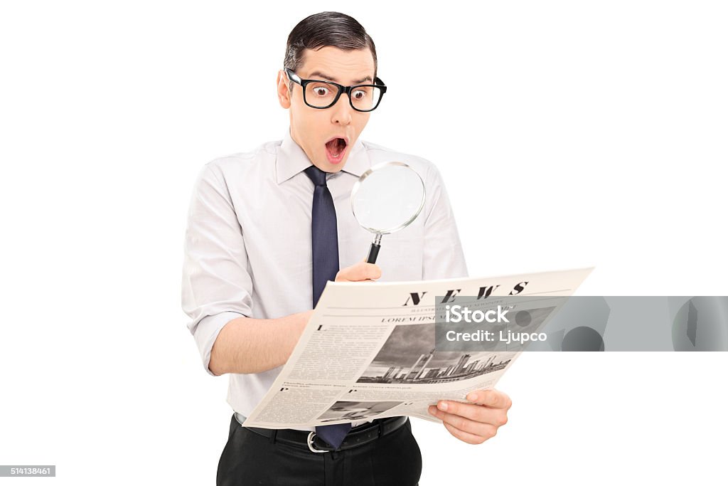 Shocked man reading the news through a magnifier Shocked man reading the news through a magnifier isolated on white background Men Stock Photo
