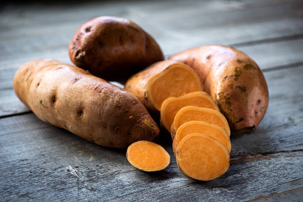 raw sweet potatoes on wooden background closeup - zoete aardappel fotos stockfoto's en -beelden