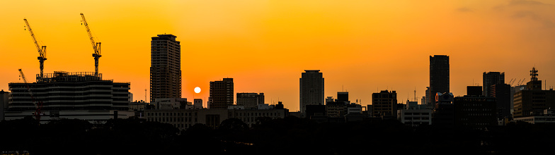 Golden sunset in burnt orange skies over the silhouetted outlines of the skyscrapers, office buildings and construction cranes of a downtown cityscape skyline in Osaka, Japan. ProPhoto RGB profile for maximum color fidelity and gamut.