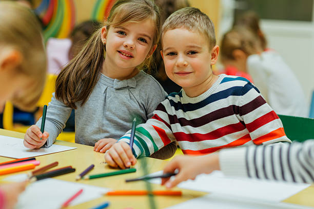 Best Friends Forever in kindergarten Portrait of two children drawing in kindergarten. They are sitting and looking at camera. Kids around are playing. Showing their imagination and skill and creativity. BFF in Kindergarten. long sleeved recreational pursuit horizontal looking at camera stock pictures, royalty-free photos & images
