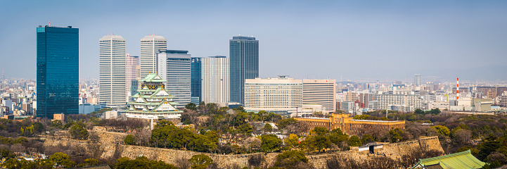 Osaka, Japan - February 28, 2016: The iconic five storey tower of Osaka Castle surrounded by the leafy foliage of Osaka Castle Park and overlooked by the modern skyscrapers of downtown Osaka, Japan's vibrant second city. Panoramic image created from ten contemporaneous sequential photographs. 