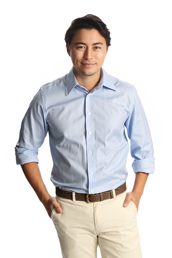 A calm relaxed man wearing a light blue shirt with beige pants, standing against a white background. Carefree and relaxed looking at camera.