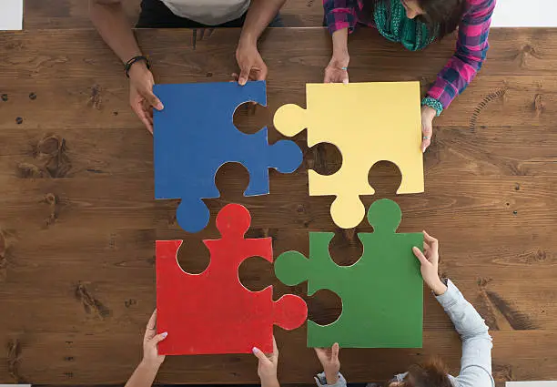 A multi-ethnic group of college age students are putting together large puzzle pieces.