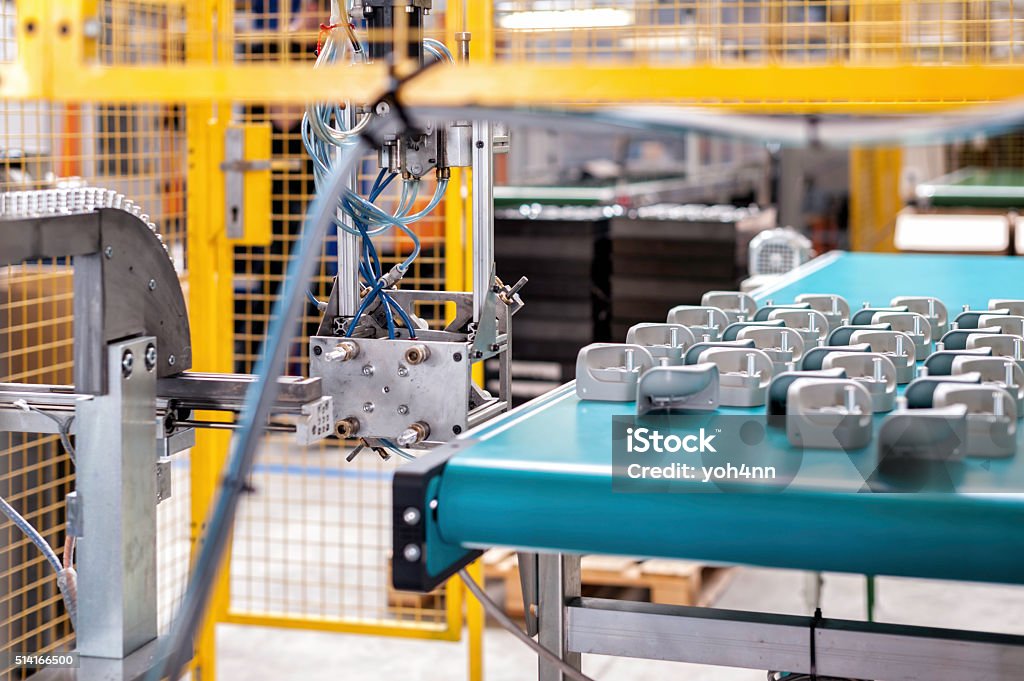 Industrial robotic arm and conveyor belt Horizontal color image of industrial robotic arm picking up the plastic pieces which are waiting in line on automated conveyor belt. Manufacturing Stock Photo