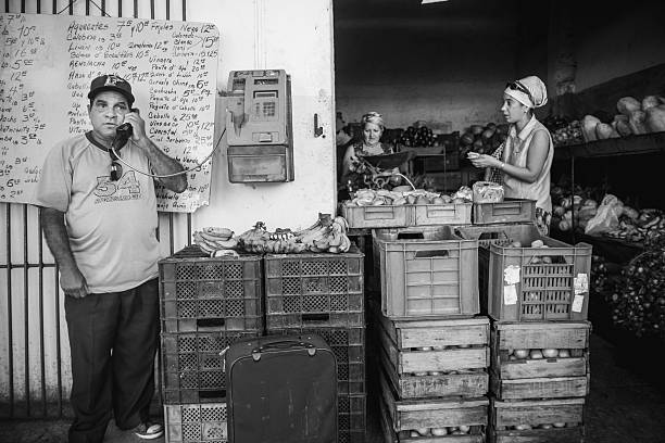 Havana, Cuba - November 10, 2015. Weekend outdoor street corner market  in Centro De Habana. Just like every Saturday before, outdoor market is in full swing, offering local neighbourhood wide variety of fresh fruits and vegetables. Women checking out the produce for sale, Man talking on the phone at the public phone boot. 
