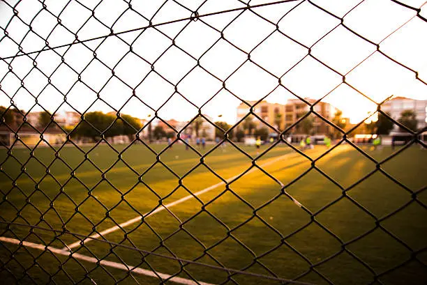 Football field behind the wire netting in the evening.