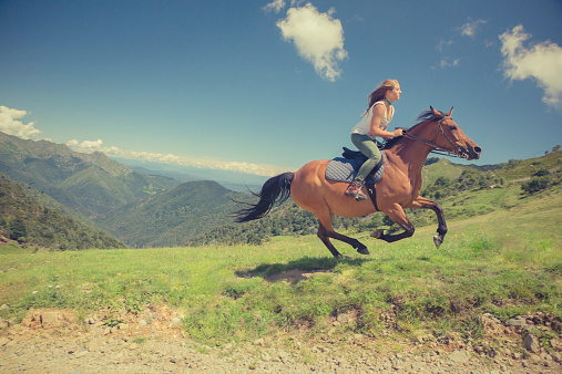Young woman with brown horse at gallop on mountain outdoor