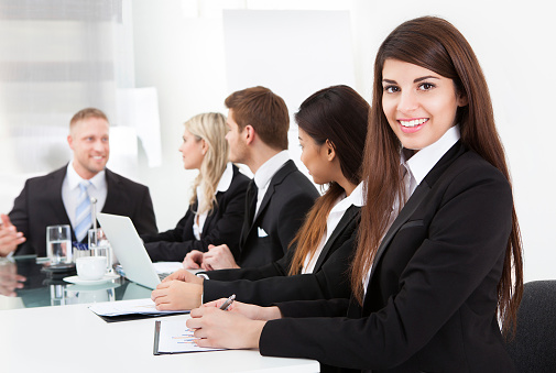 Portrait of beautiful businesswoman sitting with colleagues in meeting at office