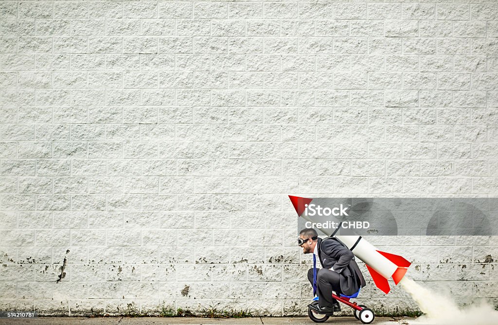 Moving forward Businessman riding a tricycle and getting help from the rocket strapped to his back :-) Rocketship Stock Photo